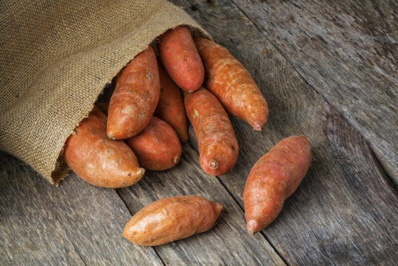 A wooden board with a bag of sweet potatoes that are spilling out