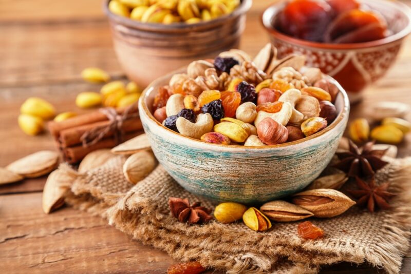 A wooden table with three bowls filled with nuts and seeds