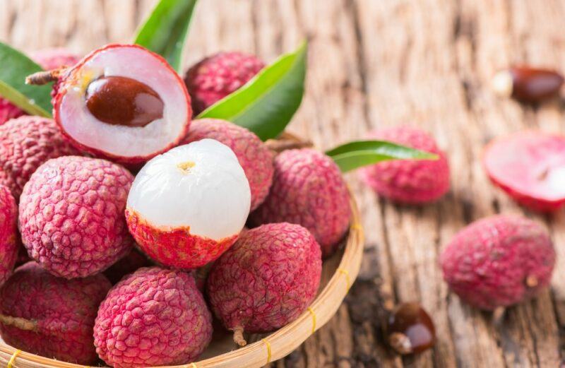 A wooden table with a bowl filled with lychees, two of which have been cut opened