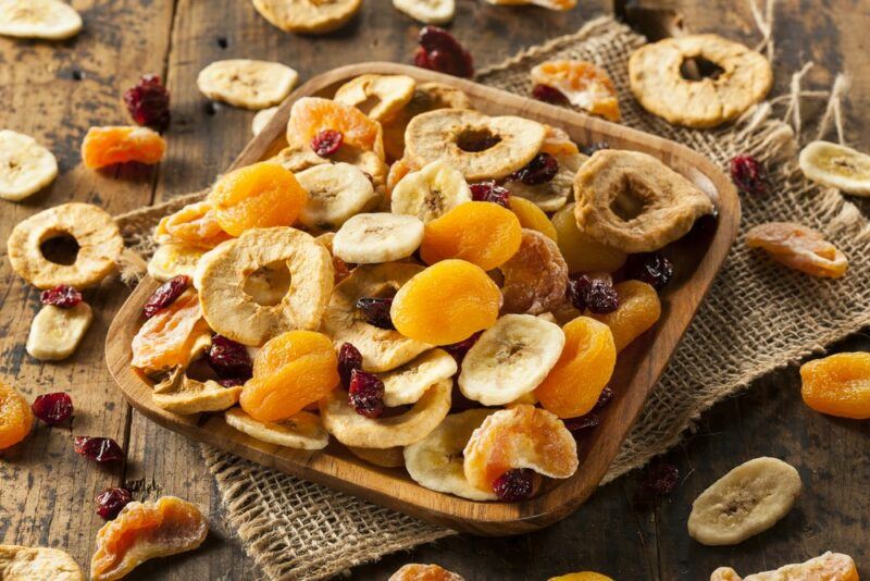 A wooden table with dried fruit scattered across it, plus a woven cloth, and a wooden plate filled with even more pieces of dried fruit