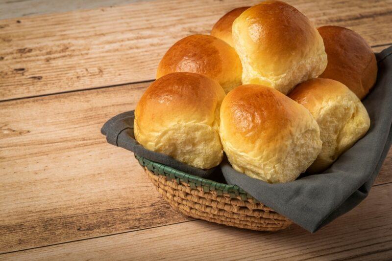 A basket with white bread rolls on a wooden table