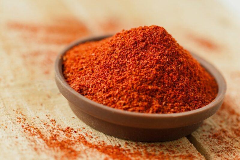 A wooden table with paprika, next to a bowl with paprika powder