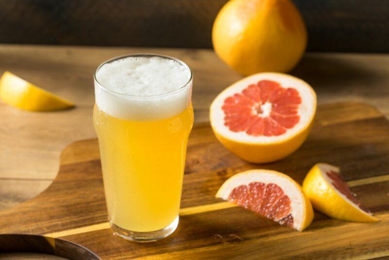 A wooden table with a pint of grapefruit shandy, next to a whole grapefruit and some grapefruit wedges