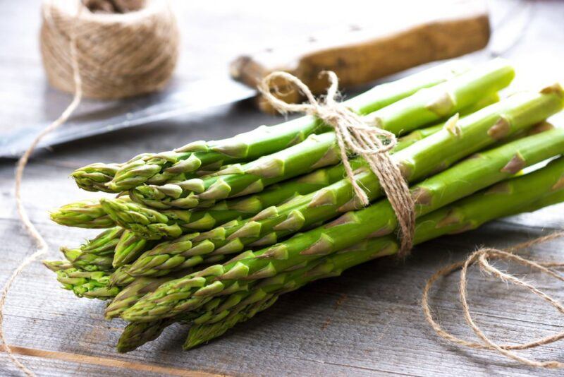 A bundle of fresh asparagus that has been tied with string, next to a knife and a ball of string