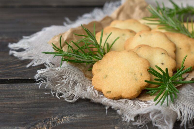 A white cloth on a wooden table with herbed shortbread cookies and some sprigs of herbs