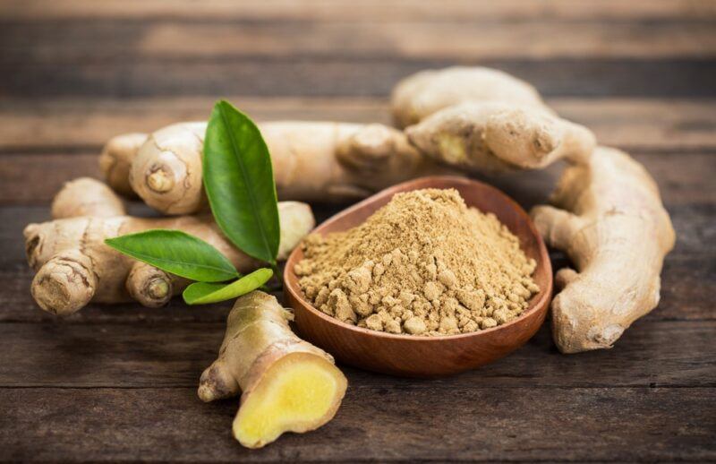 A wooden table with ginger roots and a wooden bowl of ginger powder