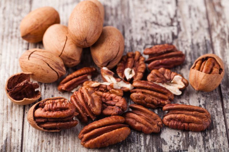 A wooden table with pecans. Some in their shells, some out of them