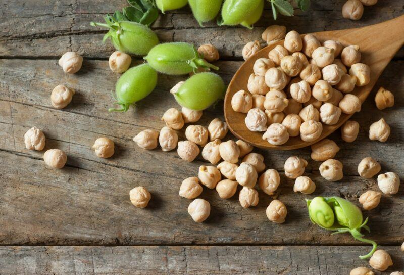 A wooden table with raw chickpeas on a wooden spoon