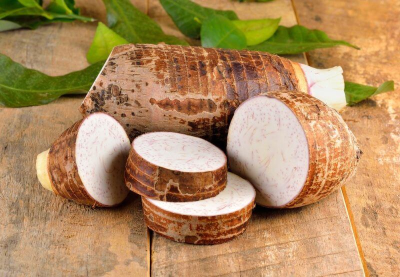 A wooden table with one whole taro root, plus thick slices of taro