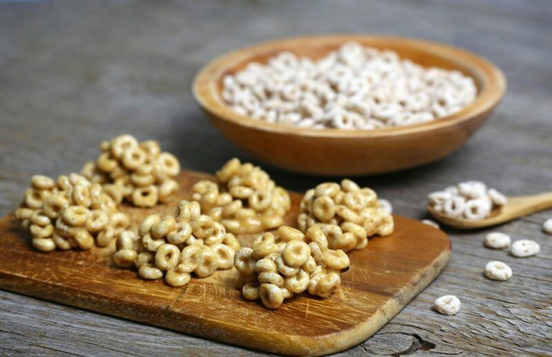 A wooden board with Cheerio-based treats, with a bowl of Cheerios in the background