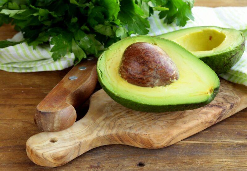 A wooden tray containing avocados with some green herbs in the background