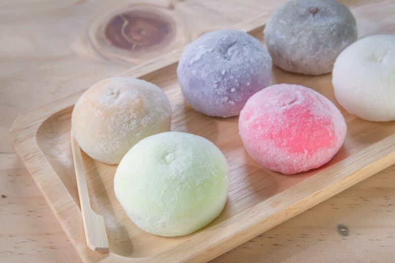 A wooden tray with six pieces of mochi ice cream, each in a different pastel color