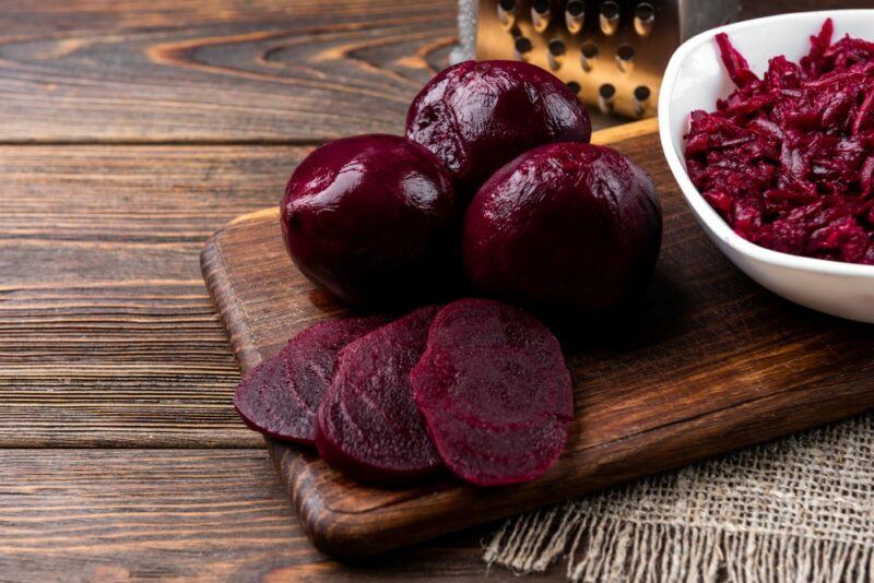 A wooden board with beets, sliced beets, and a bowl of grated beets