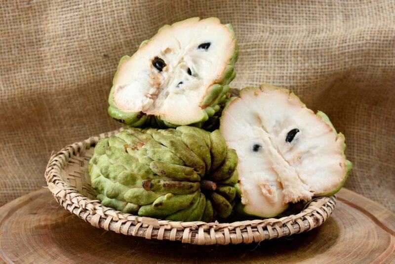 A woven dish with two atemoya halves and a whole atemoya fruit