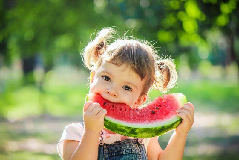 A young girl with pigtails eating a watermelon wedge