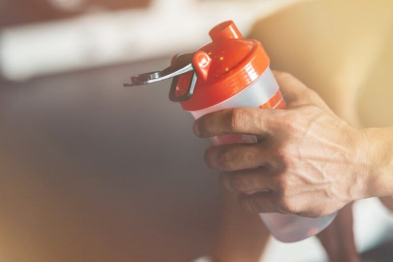 A young man holding a bottle containing a pre workout drink