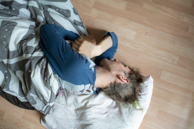 A young man sleeping on the floor with a pillow and blanket