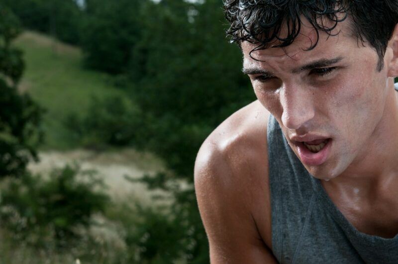 A young man who has been exercising outside and is out of breath and covered in sweat