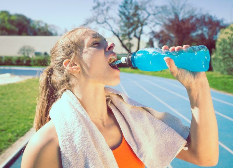 A young woman with a towel around her neck drinking blue Powerade