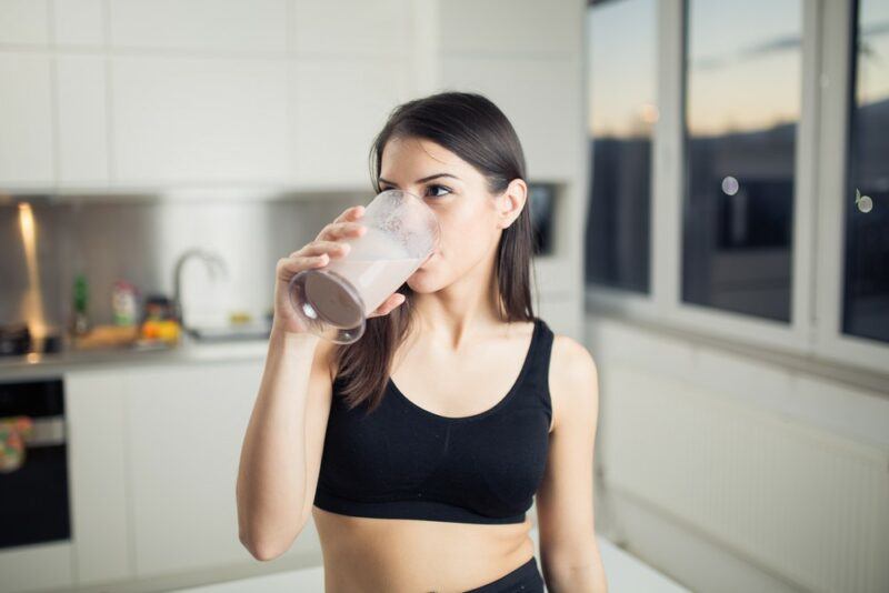 A young woman in a kitchen drinking chocolate milk | Food For Net A woman in a black sports bra drinking a glass of chocolate milk