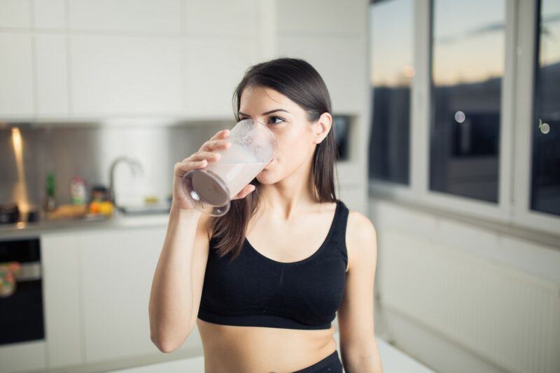 A woman in a black sports bra drinking a glass of chocolate milk