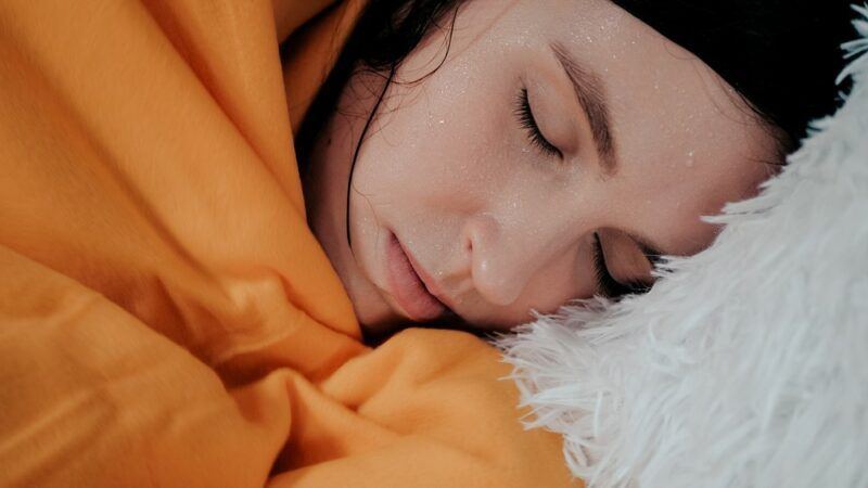 A sweating young woman lying in bed, who appears to be sick