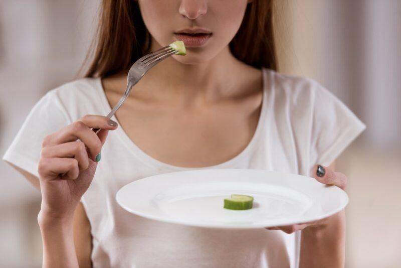 A woman holding onto a white plate with a tiny piece of food on it