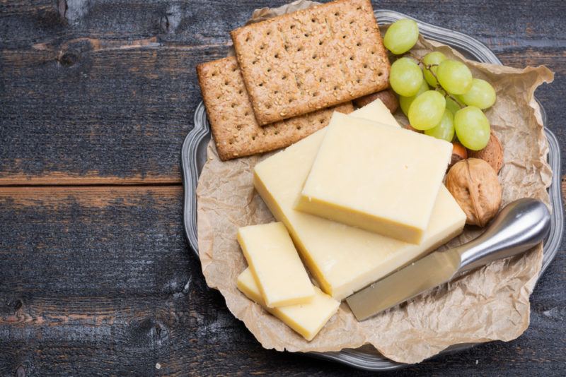 A metal tray with aged cheddar, crackers, paper, grapes and a knife