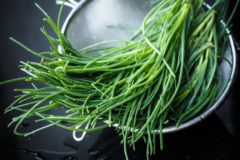 on a dark surface is a metal colander with a bunch of agretti