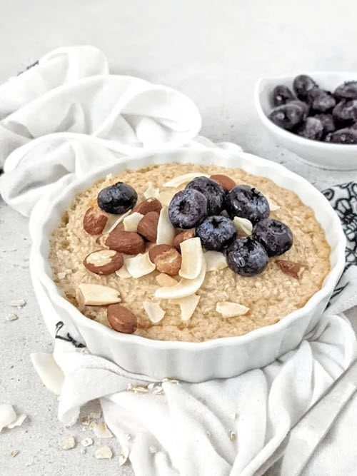 A shallow white dish of baked oatmeal, topped with nuts and blueberries