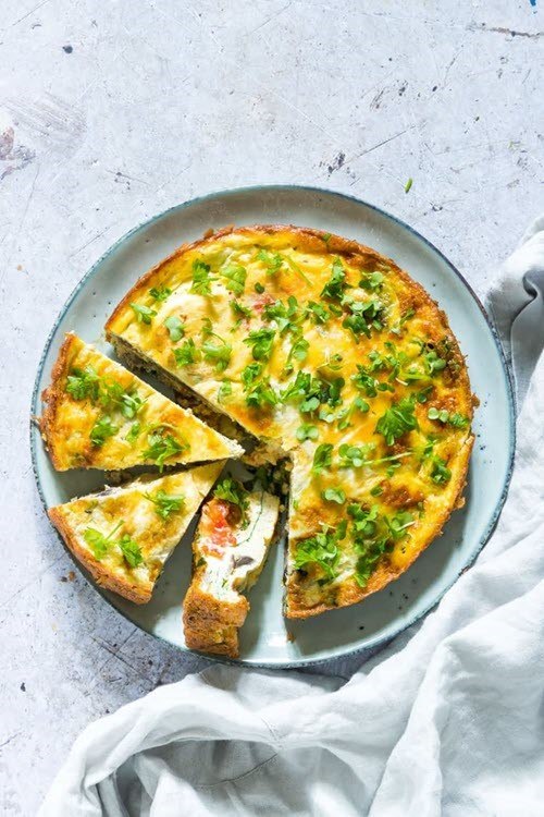 A large plate containing an air fryer breakfast frittata that has a few pieces cut out of it