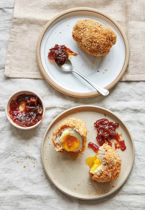 Two plates on a table, containing Scotch eggs, next to toppings