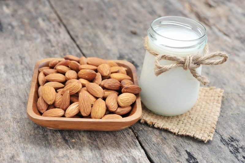 A glass jar of almond milk next to a wooden dish of almonds