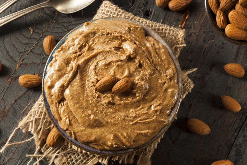 Almond butter in a large bowl surrounded by almonds