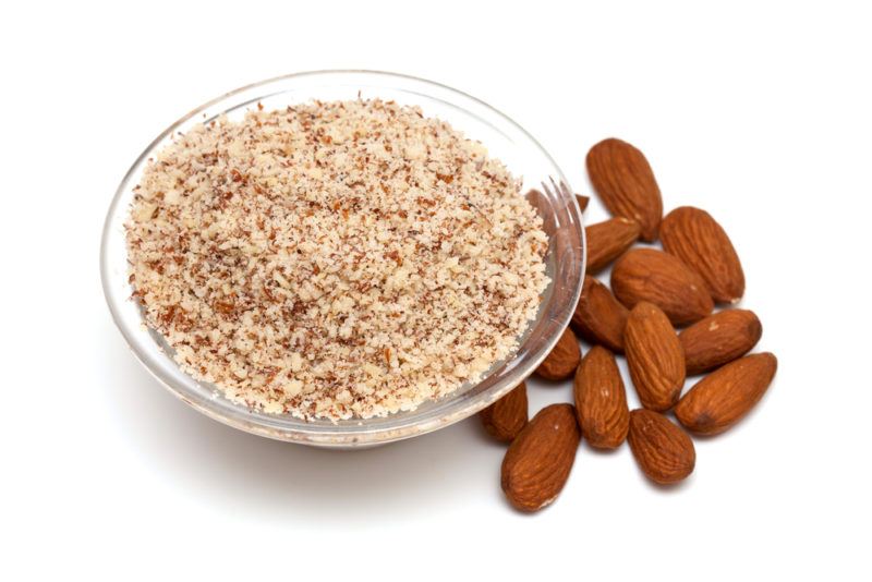 Almond meal in a bowl next to almonds