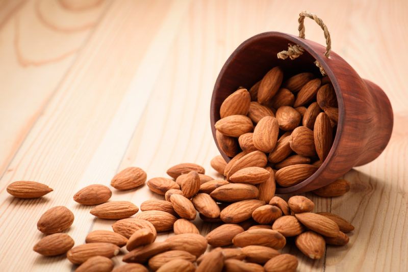 A small pail of almonds being spilled out onto a table