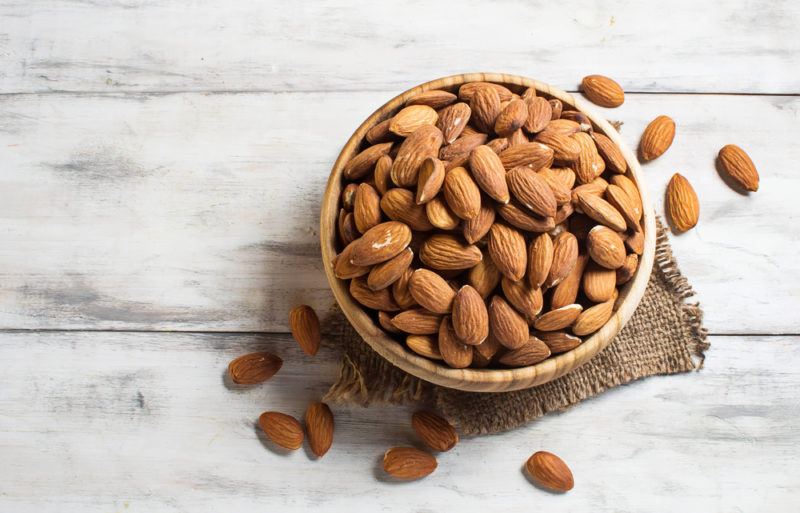 A bowl of almonds on a white wooden table