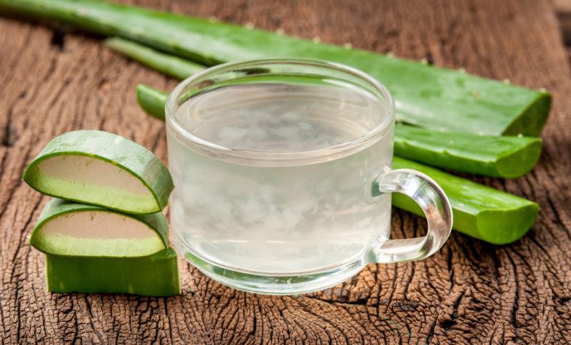 A glass mug of aloe water with variou pieces of aloe vera