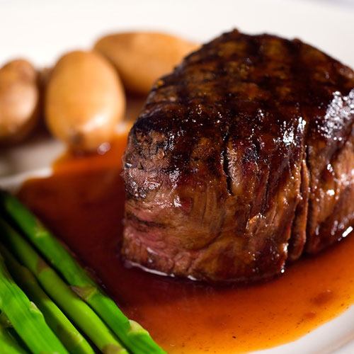 A cooked sirloin steak on a plate with potatoes and asparagus