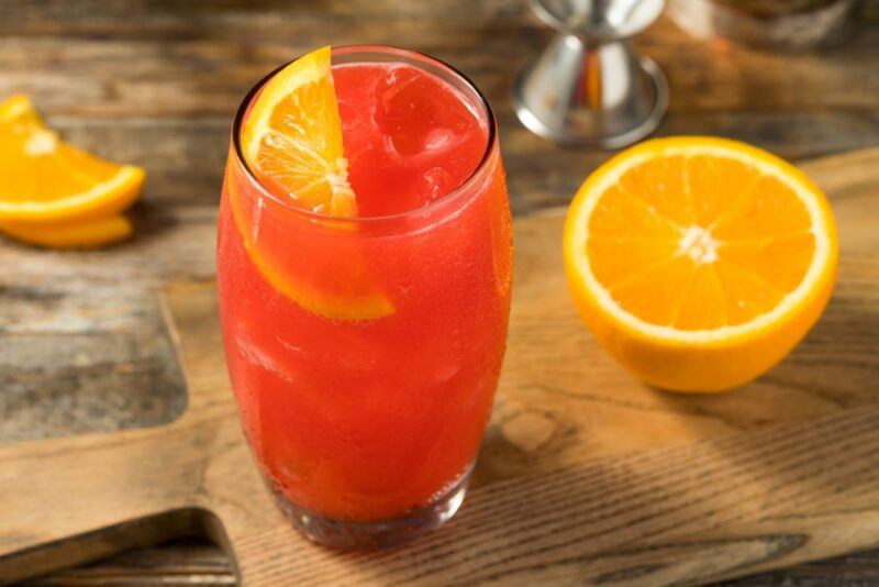 A wooden board with an Alabama slammer cocktail and half an orange, with a jigger and an orange wedge on the table