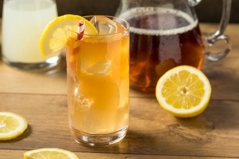 An Arnold Palmer cocktail with citrus as a garnish and iced tea in the background