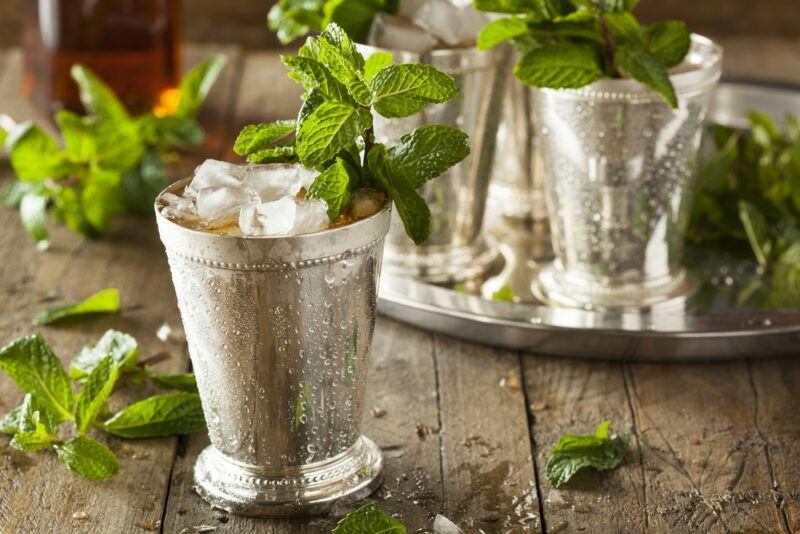 A wooden table with an Elvis cocktail that is a riff on a mint julep, next to a tray with another couple of cocktails