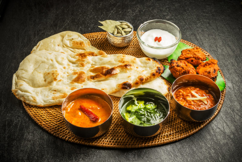 A wooden tray with naan bread, sauces, and curries