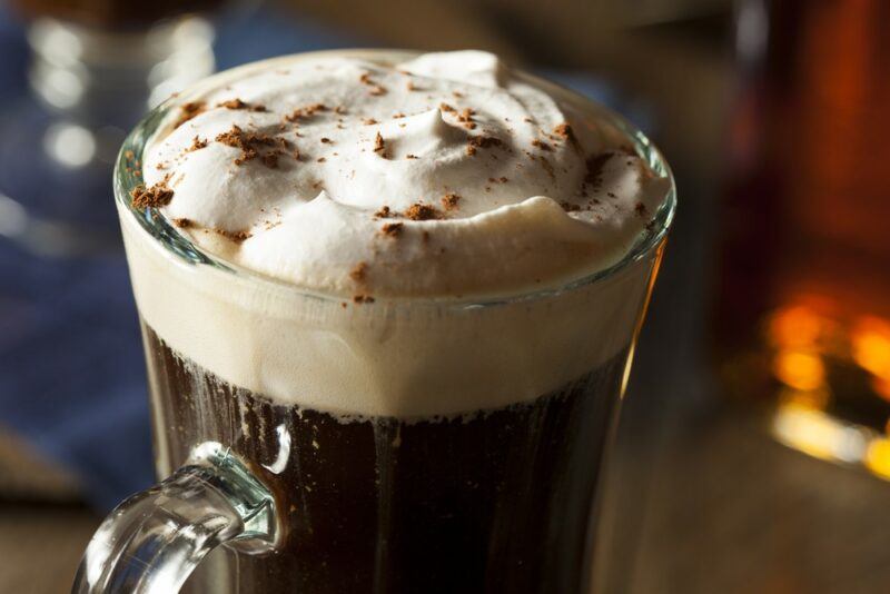 A large glass containing an Irish coffee cocktail with plenty of whipped cream on the top