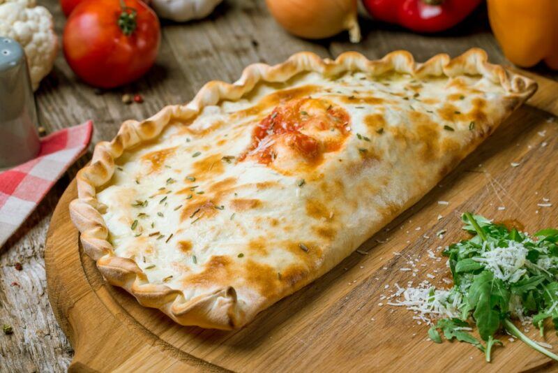 A wooden board with a large Italian calzone that's been folded over and crimped at the edges