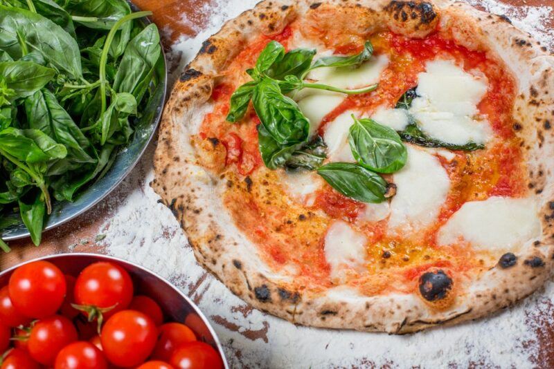 An Italian pizza on a table with tomato sauce and mozzarella cheese as toppings, next to a bowl of spinach and one of cherry tomatoes