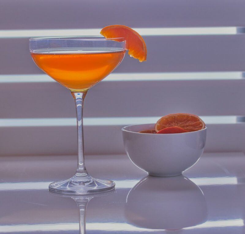 A martini glass with an Abbey cocktail and a bowl of oranges