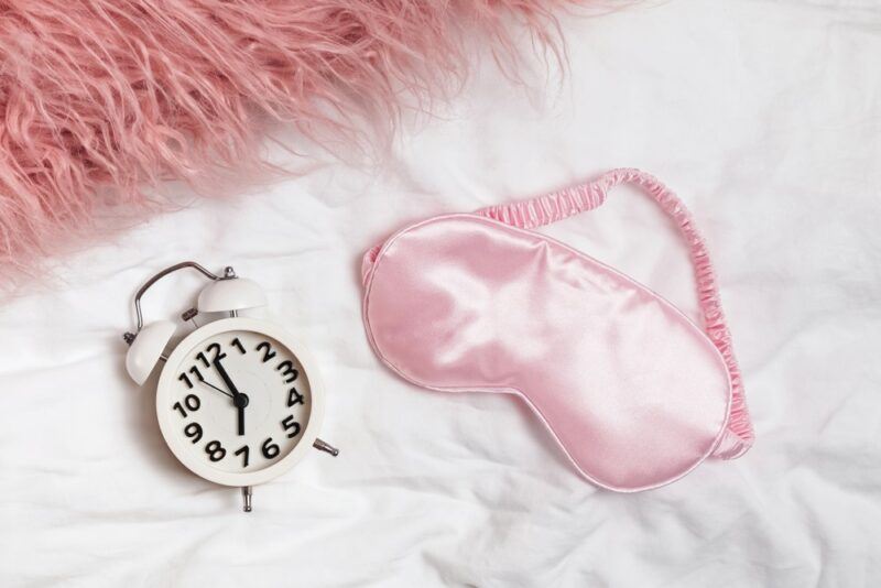 A pink eye mask next to an alarm clock and a pink rug