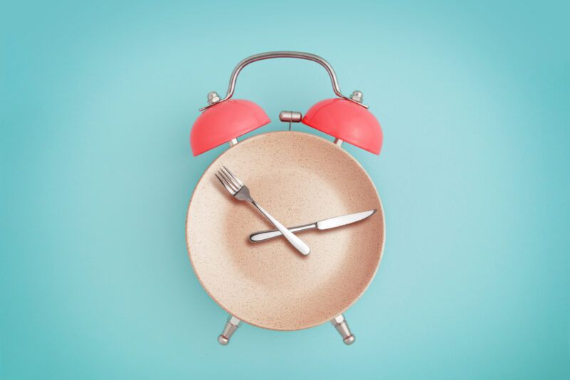 An alarm cock made using a plate, knife and fork, on a light blue background