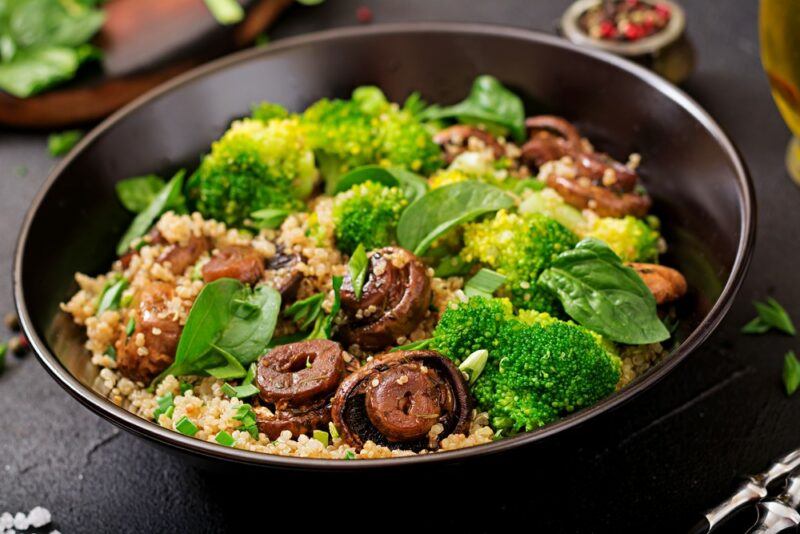 A dark bowl containing an alkaline quinoa salad with mushrooms, spinach, and broccoli